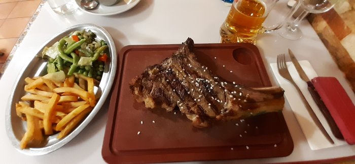 T-benstek på skärbräda med pommes frites och blandade grönsaker på sidan, ett glas öl i bakgrunden.