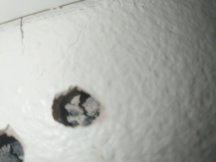 Uruholkade hål i en vitmålad vägg med en synlig spricka som tyder på tidigare arbete.