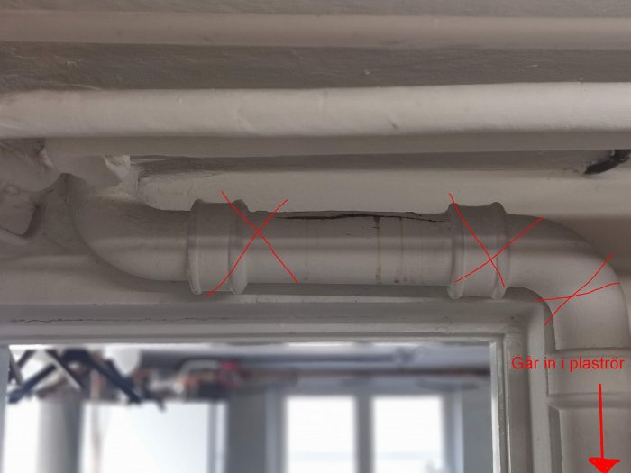 Horisontellt gjutjärnsrör med rostskador markerade med kryss, nära plaströranslutning.