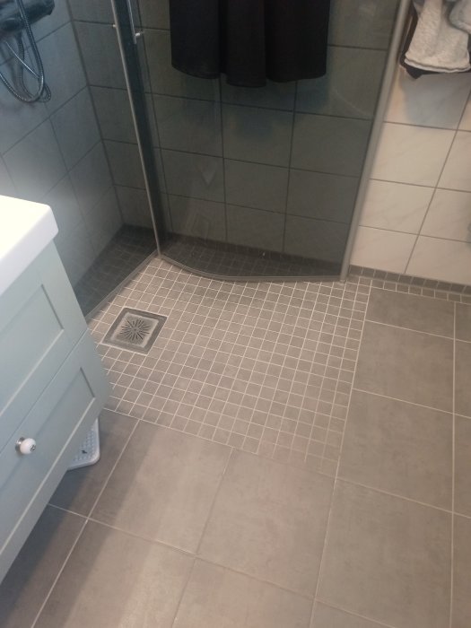 Renoverat badrum med mörkgrå storformat kakel på väggarna och mindre mosaikplattor på duschen golv.