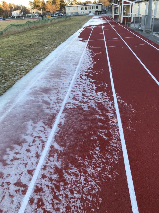 Röd löparbana täckt delvis av snö och is under vinterförhållanden.