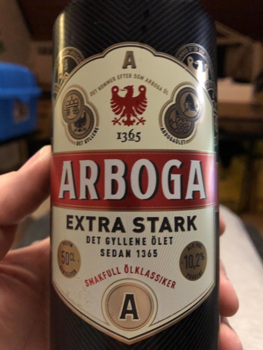 En hand som håller en burk Arboga Extra Stark öl med texten "Det gyllene ölet sedan 1365".