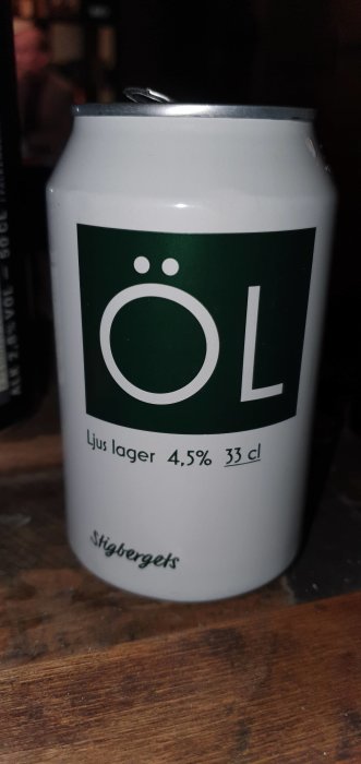 Aluminiumburk av ljus lager öl med etikett "ÖL" och detaljer 4.5% volym 33 cl, på ett träbord.