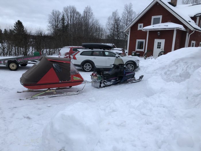 Röd stuga med snöskoter framför och släpvagn i vinterlandskap.