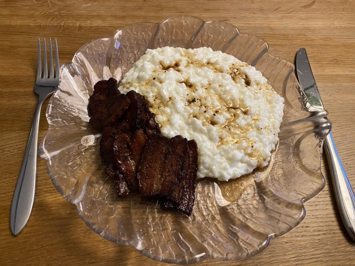 En tallrik med stekt fläsk och gröt, serveras utan dryck, på ett trämönstrat bord.