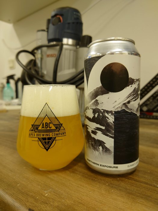 Ölglas med logotypen "ABC" fyllt med DIPA, brevid en burk märkt "Northern Exposure".