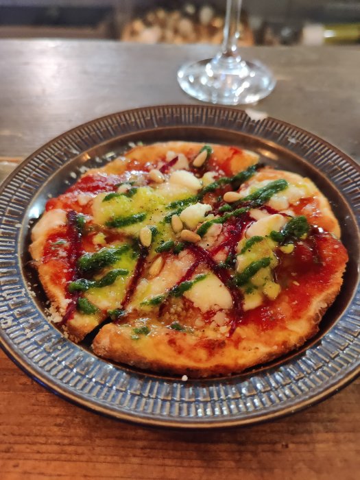 En Chevre pizza med tomatsås, ost och pesto garnityr på en blåmönstrad tallrik.