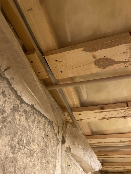 Pelare med två reglar ovanför betongbalk och plankor fastspikade underifrån i en byggkonstruktion.