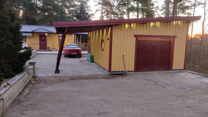 Gult isolerat garage med tillhörande carport och sedumtak vid skymning.