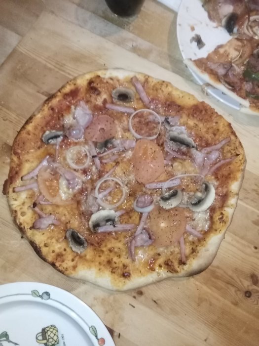 Hemgjord pizza med tonfisk, svartpeppar, lökringar och champinjoner på ett träbord.
