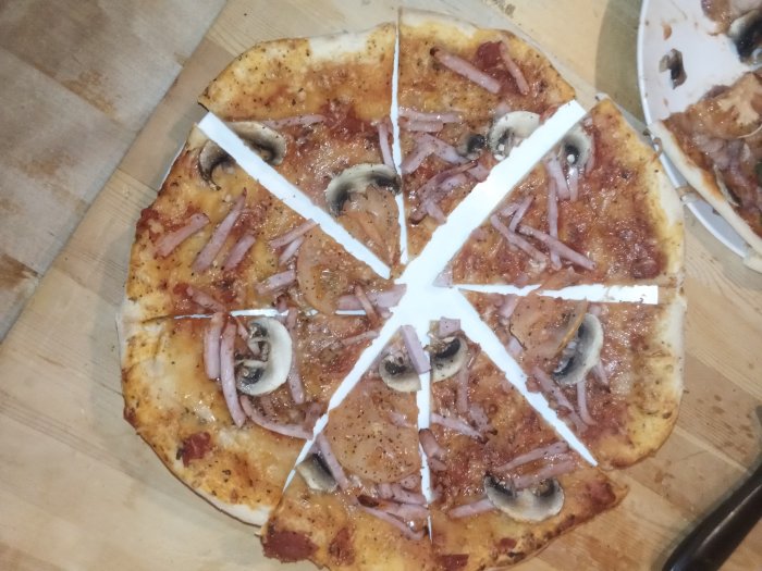 Hemlagad pizza med skinka, svamp och rödlök på ett träskärbräda.