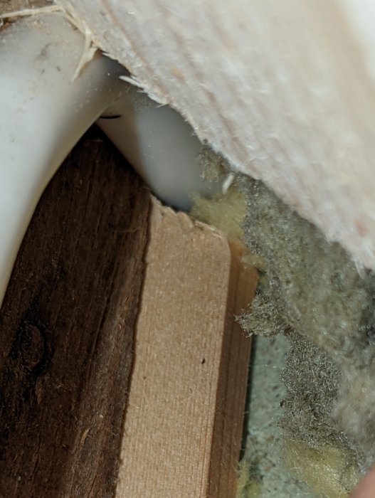 Närbild på en rörinstallation genom en vägg med isolering och trämaterial som syns.