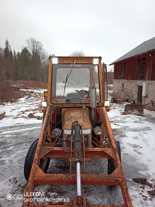 En rostig grävmaskin framför en ladugård med smältande snö på marken.