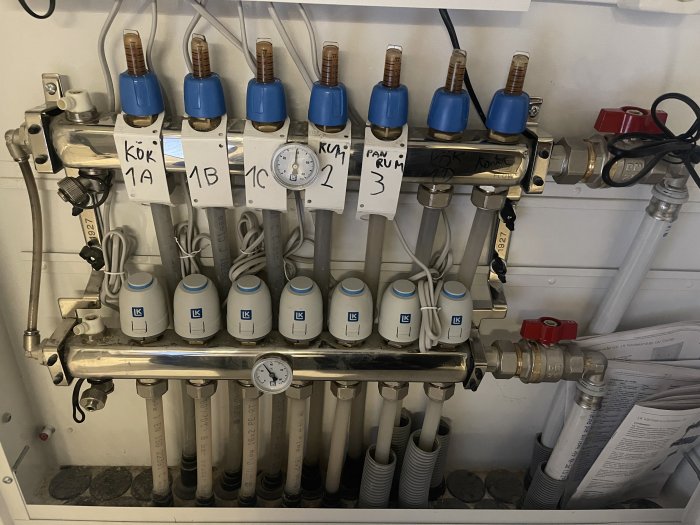 Värmefördelningssystem med etiketterade termostatventiler och rör samt en manometer.