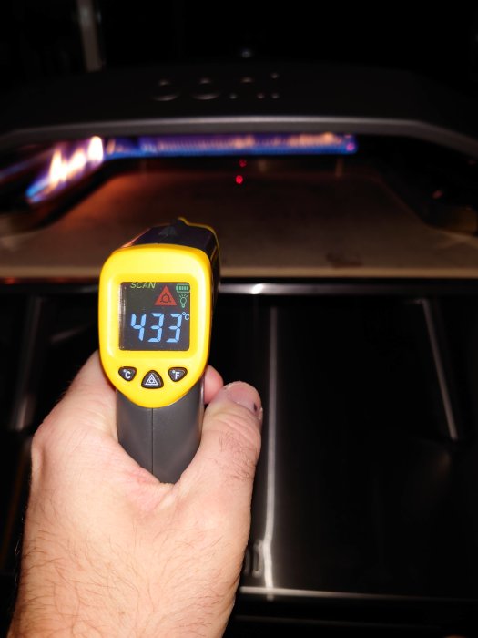 Hand håller en IR-termometer som visar 433 grader framför en igångsatt pizzaugn.