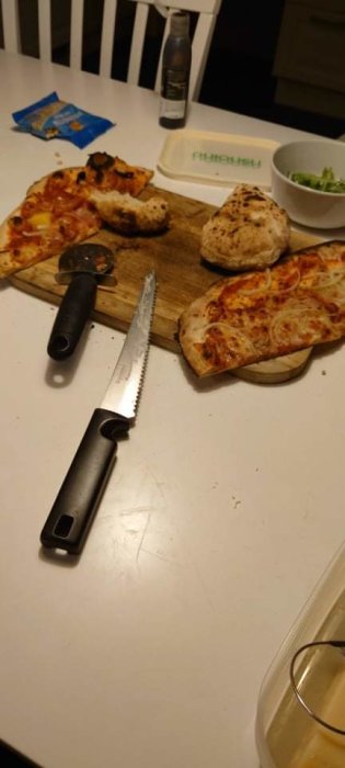 Hembakad pizza och ett försök till kebabbröd på en träskärbräda, pizzaslicer och dryck på ett matbord.