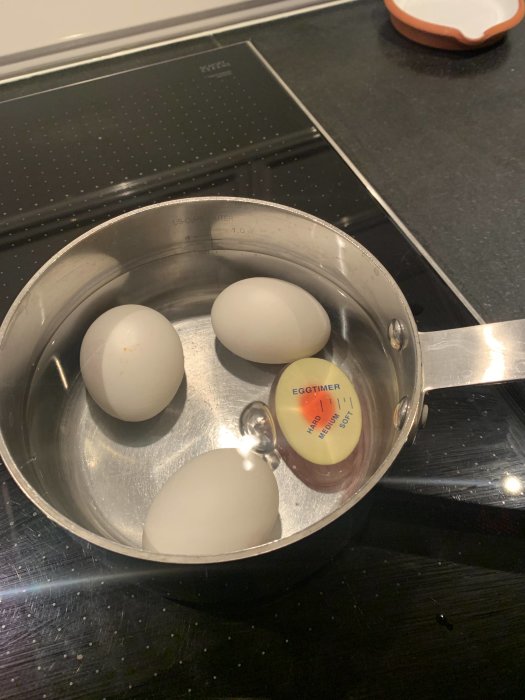 Ägg i kastrull med en äggtimer bland dem på spishäll.