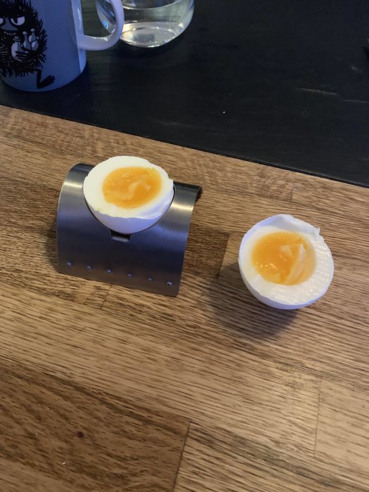 Delvis skalade, mjukt kokta ägg i ägghållare på träbord, ett med flytande gula.