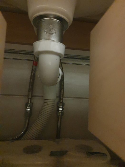 Rörsystem under tvättställ med modern gummifilterinstallation och flexibla tilloppsslangar.
