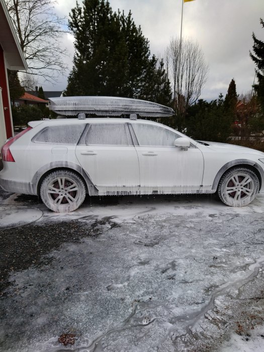 Vit Volvo täckt av tvättmedel under biltvätt på en isig uppfart.