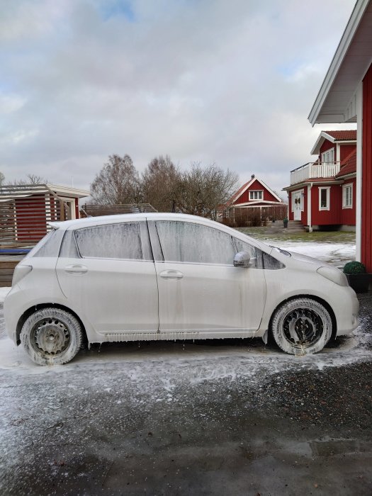 Halvtvättad bil täckt av skum framför hus, representerar Toyotan som krävde svampbehandling.