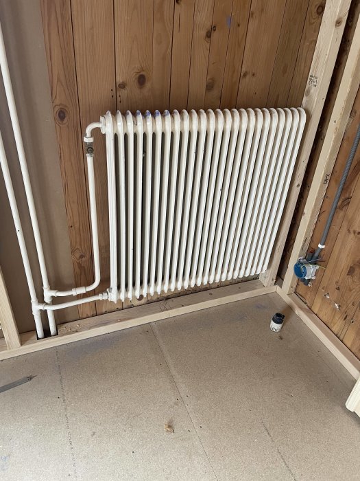 Demonterad vit radiator monterad på en trävägg i ett rum under renovering.