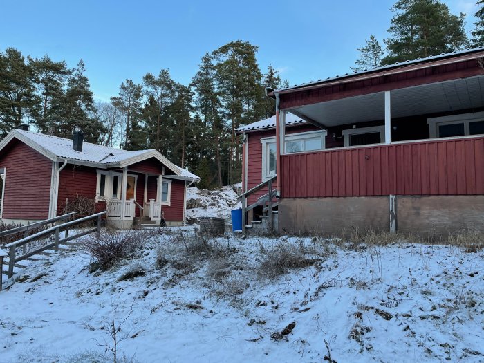 Två röda hus på en snötäckt tomt med barrskog i bakgrunden.