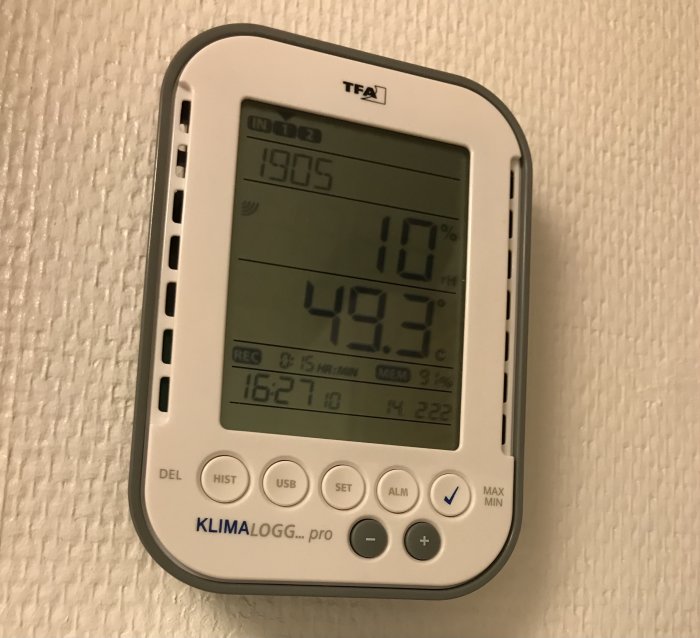 Digital hygrometer som visar 10% luftfuktighet och 49.3°C temperatur på en strukturerad vit vägg.