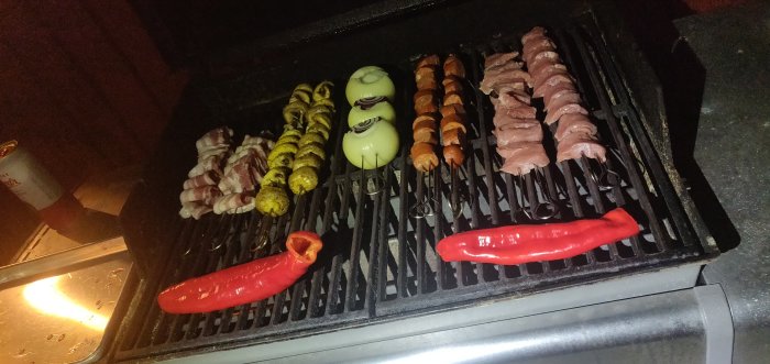 Grill med olika spett inklusive grönsaker och kött samt hel paprika och vitlöksklyftor.