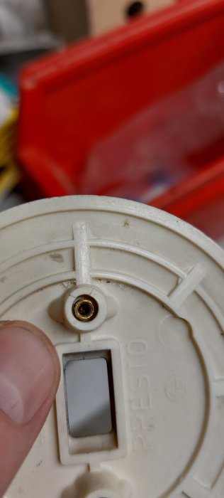 Närbild på en specialskruv med invändig gänga fästad i ett vitt plastlock hållet av en person.