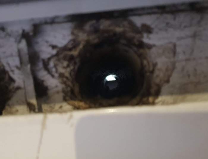 Ventilationshål i vägg som sluttar neråt, visar smuts runt öppningen och skyddsplåt syns ej.