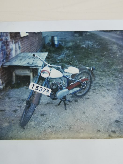 Vintage motorcykel parkerad på grus framför tegelbyggnad.