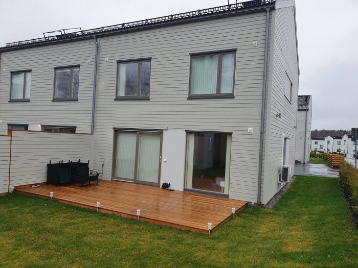 Nybyggt parhus med en angränsande träaltan på våt gräsmatta.