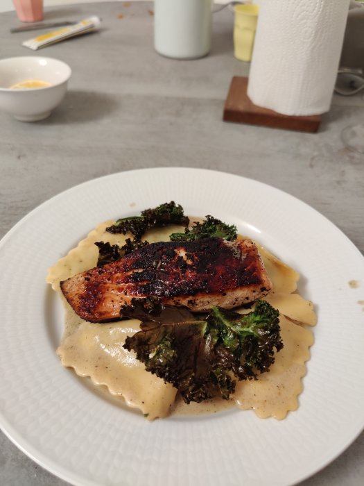 Rostad laxfilé ovanpå pasta med gräddsås och krispig grönkål på en vit tallrik.