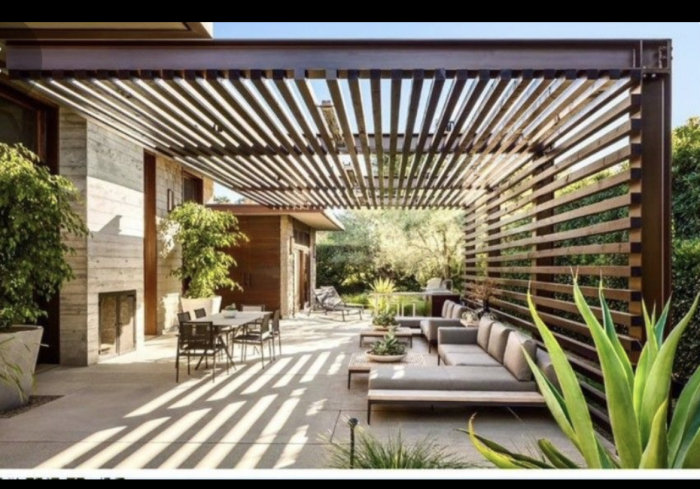 Moderna pergola med horisontella lameller som skapar skugga över en uteplats med sittgrupp.