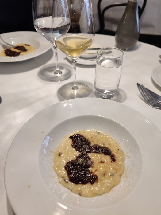 Anklever och tryffel-risotto med fikonsås serverad på en vit tallrik, med vin och vattenglas i bakgrunden.