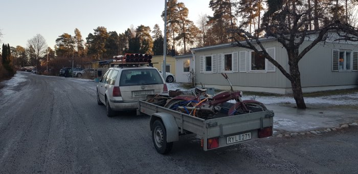 Bil fullastad med byggmaterial och verktyg drar släpvagn med gammal motorcykel.