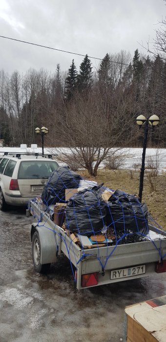 Lastad släpvagn med material täckt av presenning säkrad med nät, redo för helgens byggprojekt.