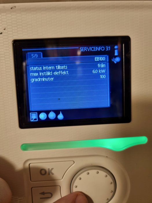 Skärm på värmepumpens kontrollpanel som visar serviceinformation och status, med en grön lysande indikator nedanför.