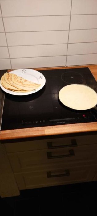 Pannkakor på en tallrik bredvid en stekpanna på en spishäll, antydan om veckans traditionell rätt.