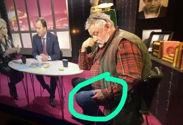 Man i rutig skjorta och väst sitter och ser disträ på sin telefon, ignorerad av övriga i studion.