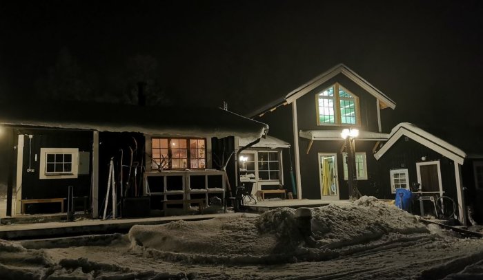 Tvåplanshus i vinternatt med belysning, snötäckt mark och synliga byggdetaljer.