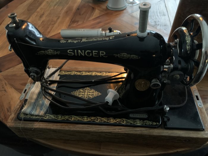 Gammal svart Singer symaskin modell 66 med guldfärgade dekorationer i trälåda, tillverkad 1927.