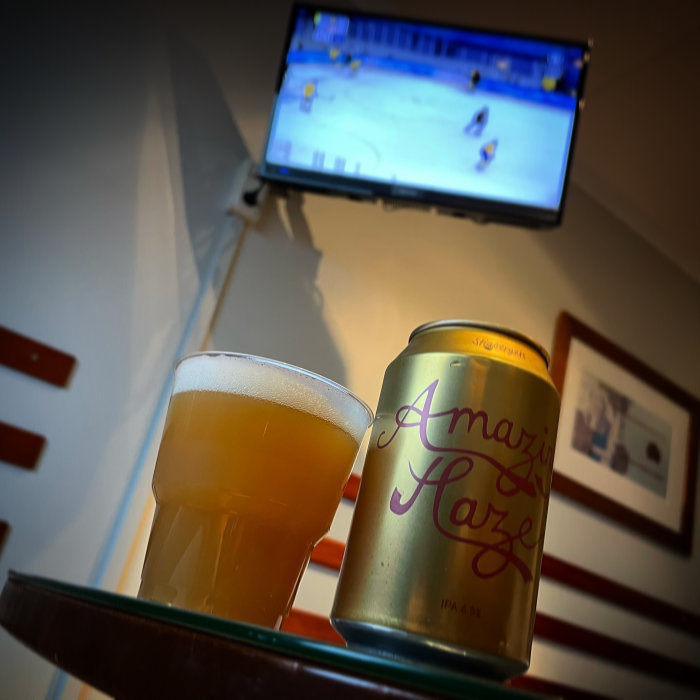 Ölglas och ölburk på bord med ishockeymatch på TV i bakgrunden