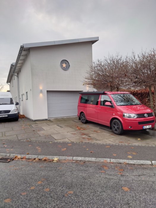 Vit husfasad med garage och dekorativ stjärna, röd Volkswagen-buss parkerad framför.