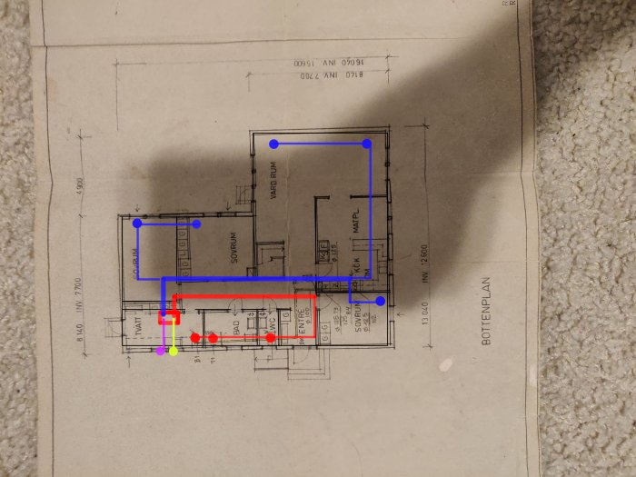 Husritning med markerade luftkanaler i blått och rött, samt punkter i gult och rött, ligger på en matta.