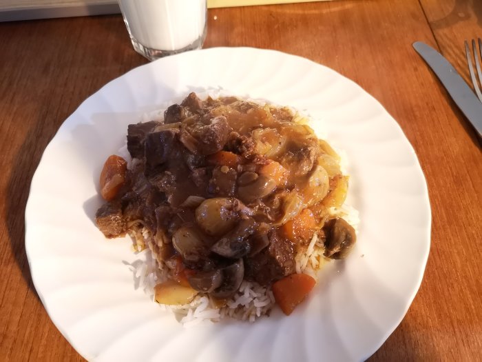 Boeuf bourguignon serverad på en bädd av ris på en vit tallrik.