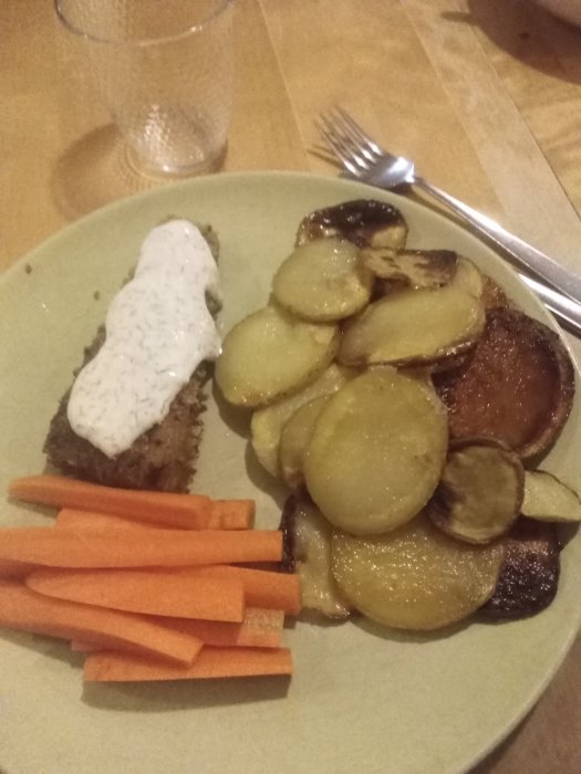Hemlagad fish and chips med stekt fisk, potatis, morotsstavar och vit sås på en tallrik.