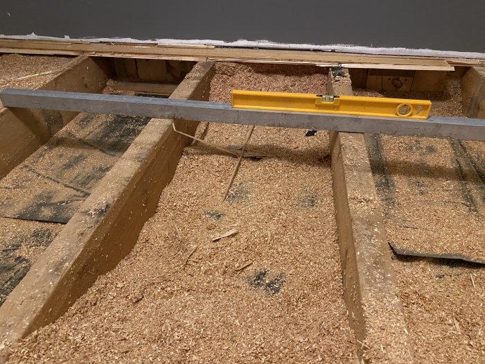 Vattenpass på exponerade golvbalkar med sågspån under renovering av golv.