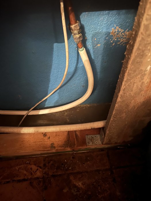 Rörinstallation i källare med läckage, inbegripet koppar- och plastledningar mot blå vägg och tegelgolv.